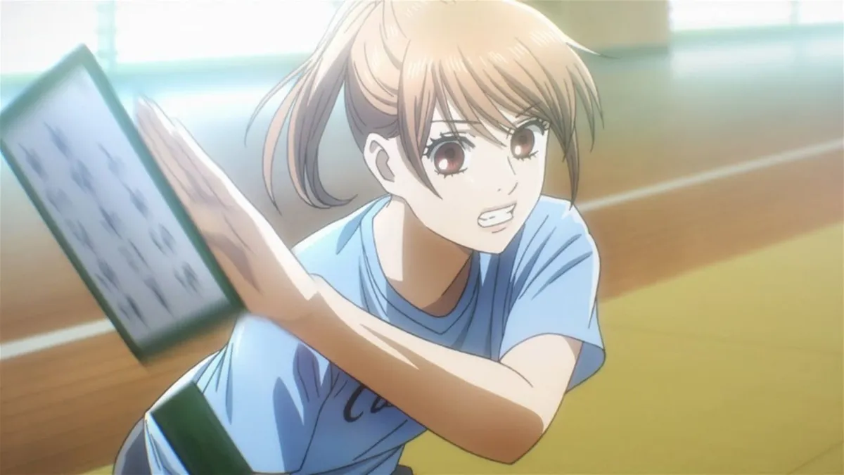 Chihaya, in a blue T-shirt with her hair tied back, lunges across the mat to swipe a karuta card, in a still from Chihayafuru